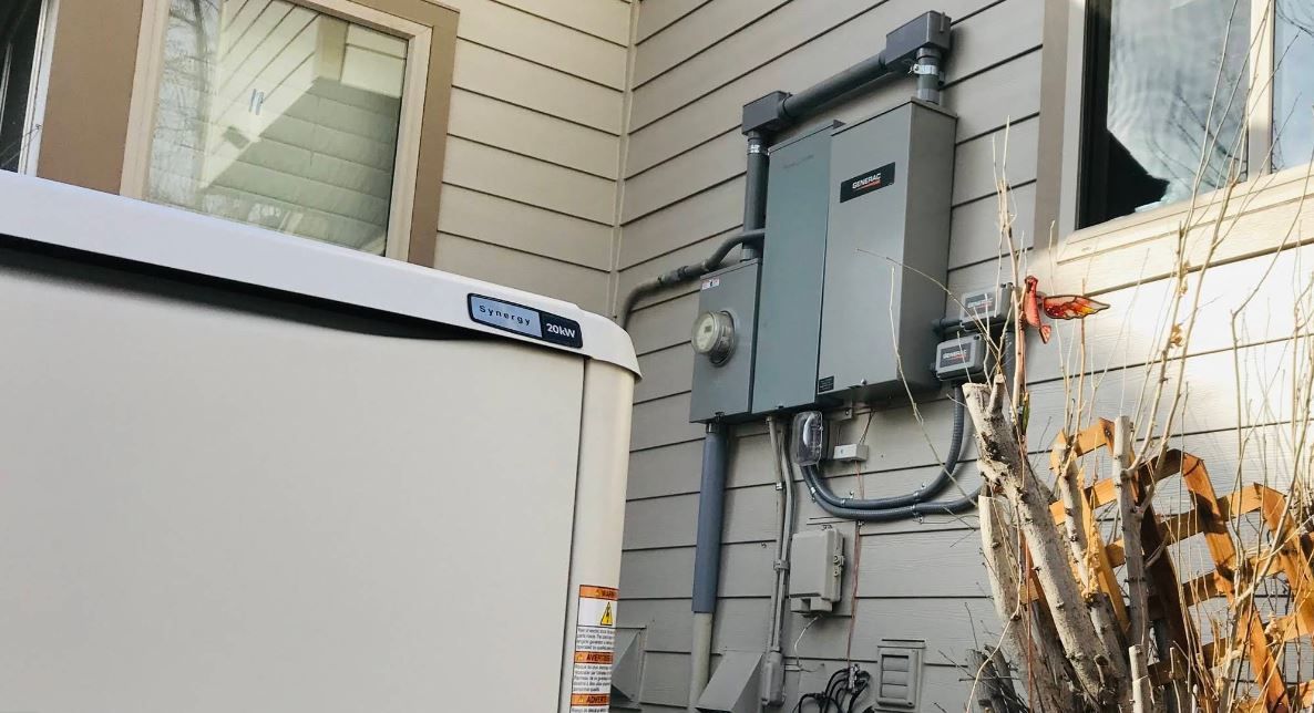 A white box is sitting on the side of a house next to a window.