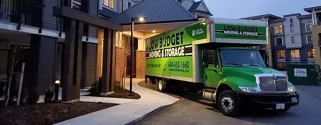 A green moving truck is parked in front of a building.