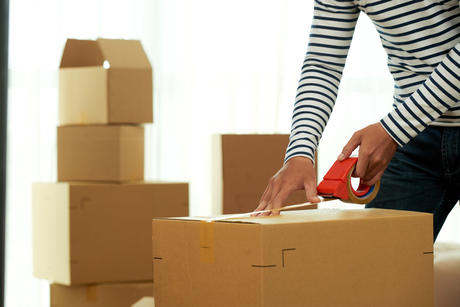 A person is taping a cardboard box with red tape.