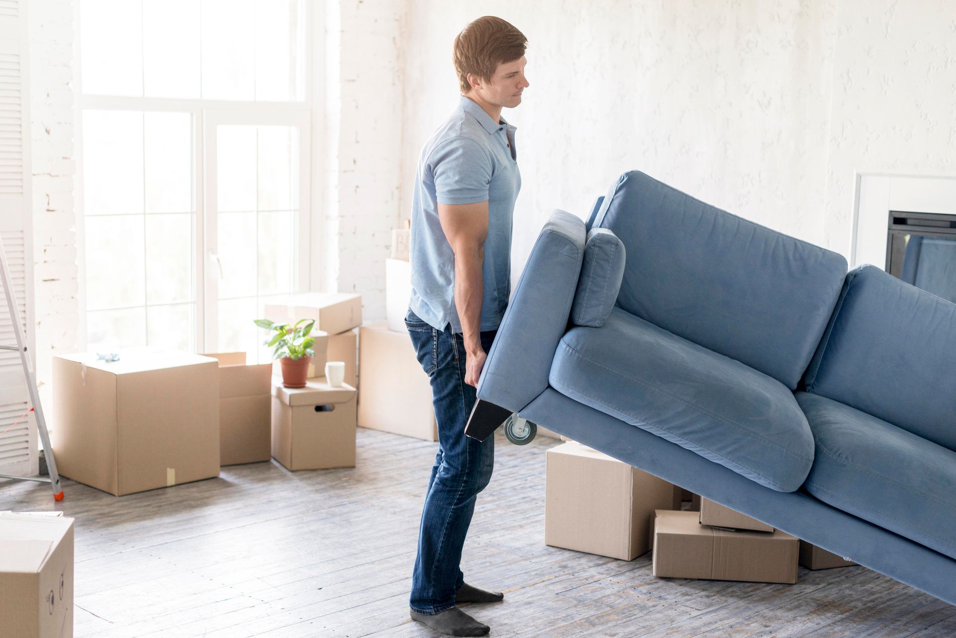 A man is carrying a blue couch in a living room.