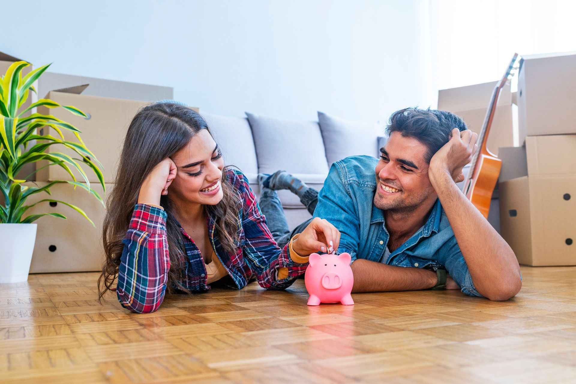 A man and a woman are laying on the floor looking at a piggy bank.