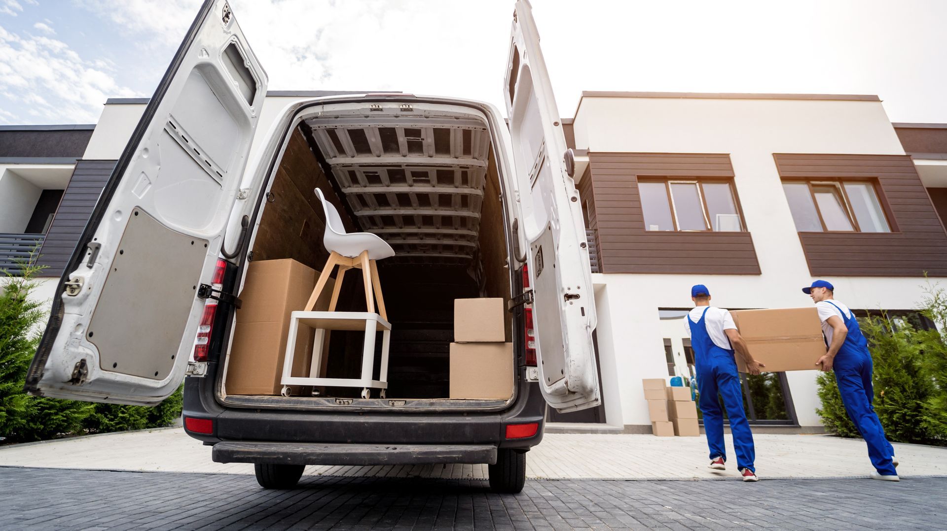 Two movers are loading a van with boxes in front of a house.