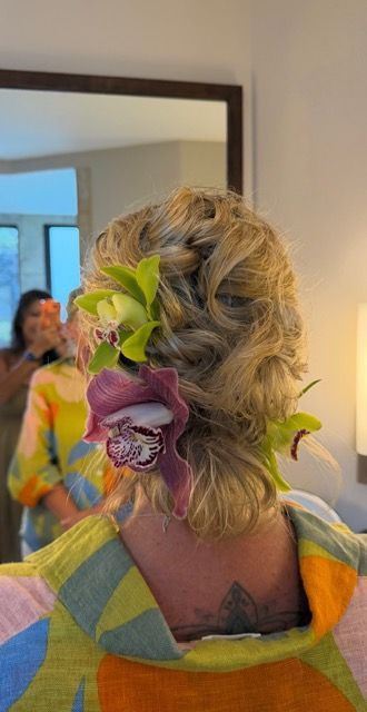 Woman with blonde updo and green-purple flowers, seen from behind in a mirror
