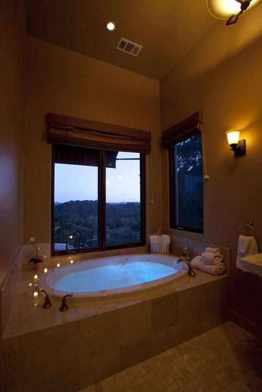 Cozy bathroom with lit candles around a soaking tub, overlooking a forest view.