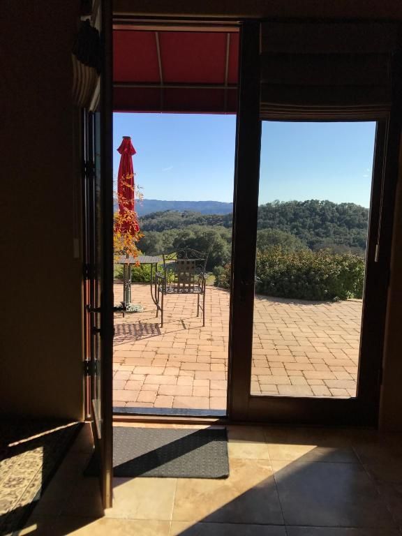 Open doorway with a view of a patio with tables and chairs, umbrella, and a landscape with trees.