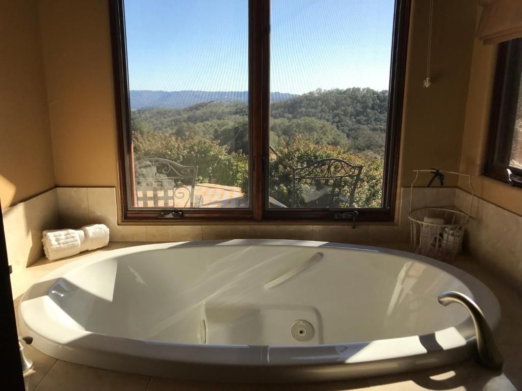 Bathroom with a large oval tub by a window with a view of green hills and a blue sky.