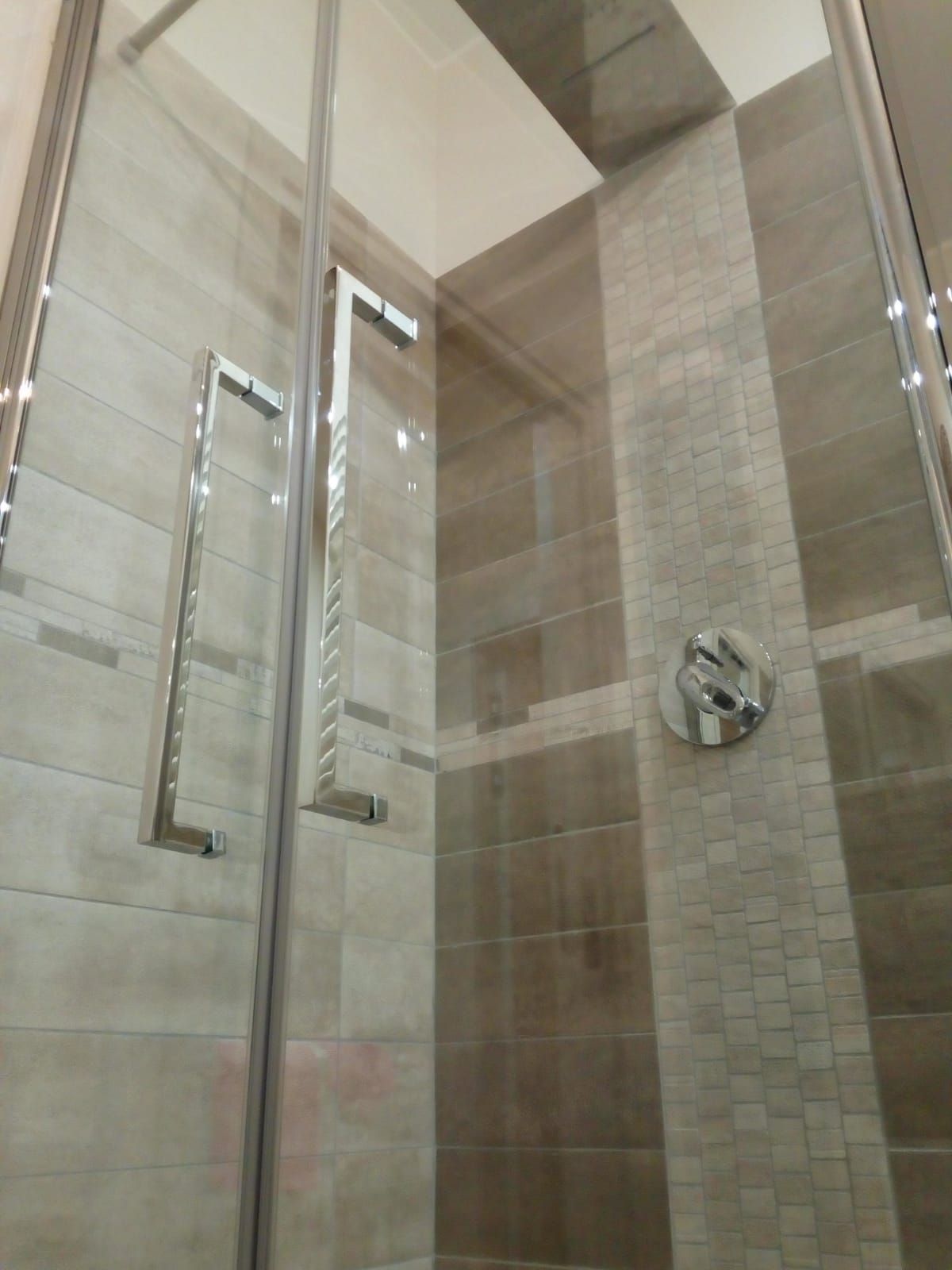 una doccia con porte in vetro e piastrelle marroni