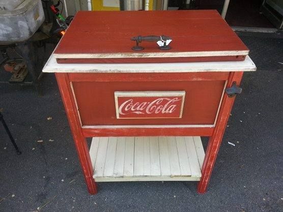 Red Coca-Cola chest-style cooler on a white shelf with a metal latch and handle.