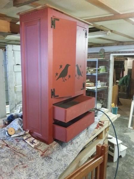 Red wooden cabinet with drawers and black bird stencil, sitting on a cluttered workbench in a workshop