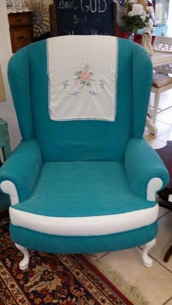 Teal upholstered armchair with white trim and a floral cloth draped over the back, on a patterned rug.