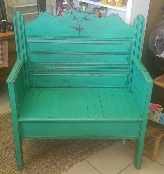 Turquoise wooden bench with a slatted back and painted decorative top, shown indoors on a carpeted floor.