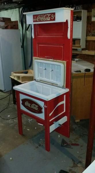 Red Coca-Cola branded chest cooler and display cabinet standing in a workshop or garage.
