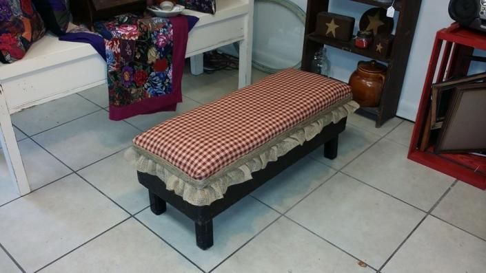 Padded bench with red checkered cushion in a tiled room near shelves and decorative items