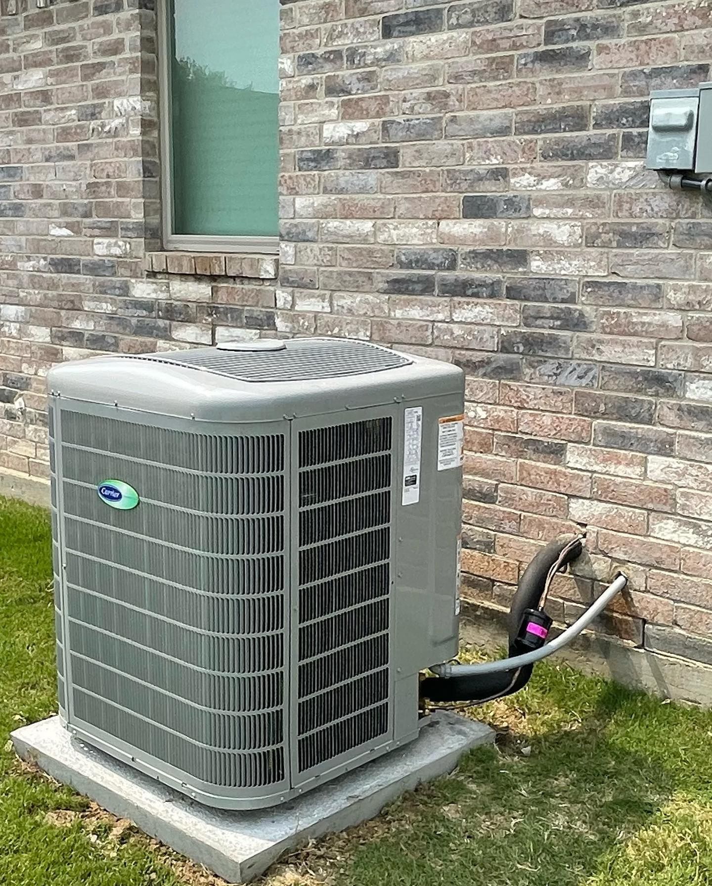 An air conditioner is sitting on the side of a brick building.