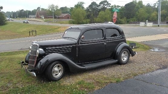 An old black car is parked on the side of the road.