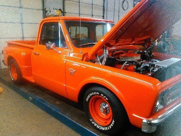 An orange truck with the hood up is parked in a garage