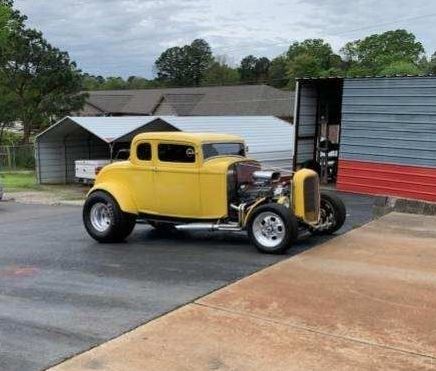 A yellow hot rod is parked in a parking lot in front of a building.