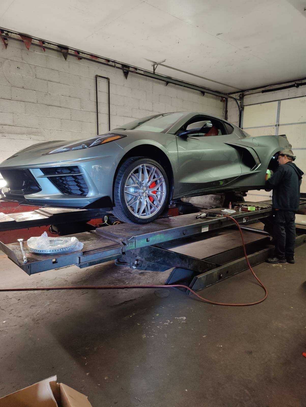 A man is working on a corvette on a lift in a garage.