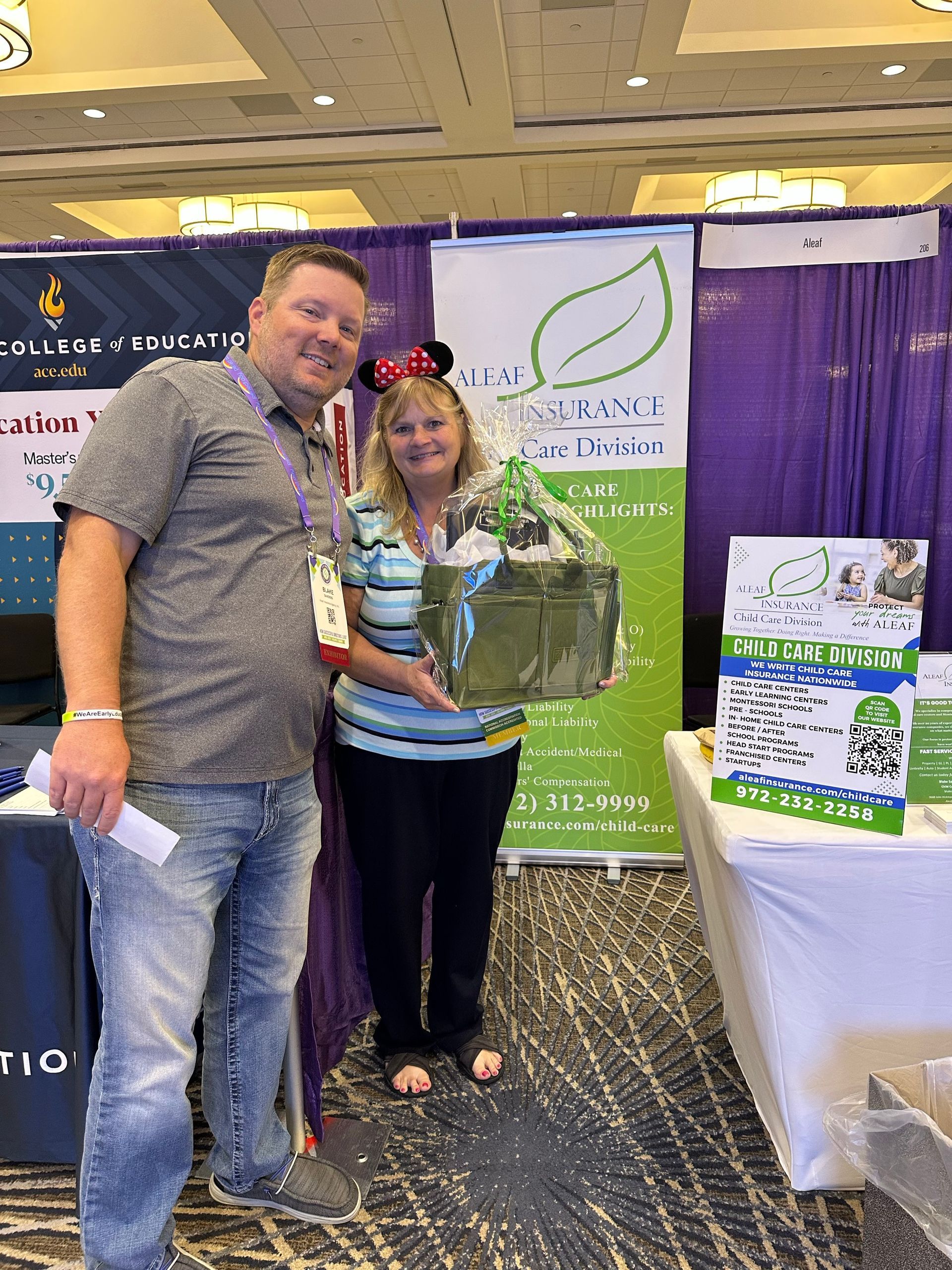 Man and woman at a booth; woman holding a gift basket, wearing Mickey Mouse ears.
