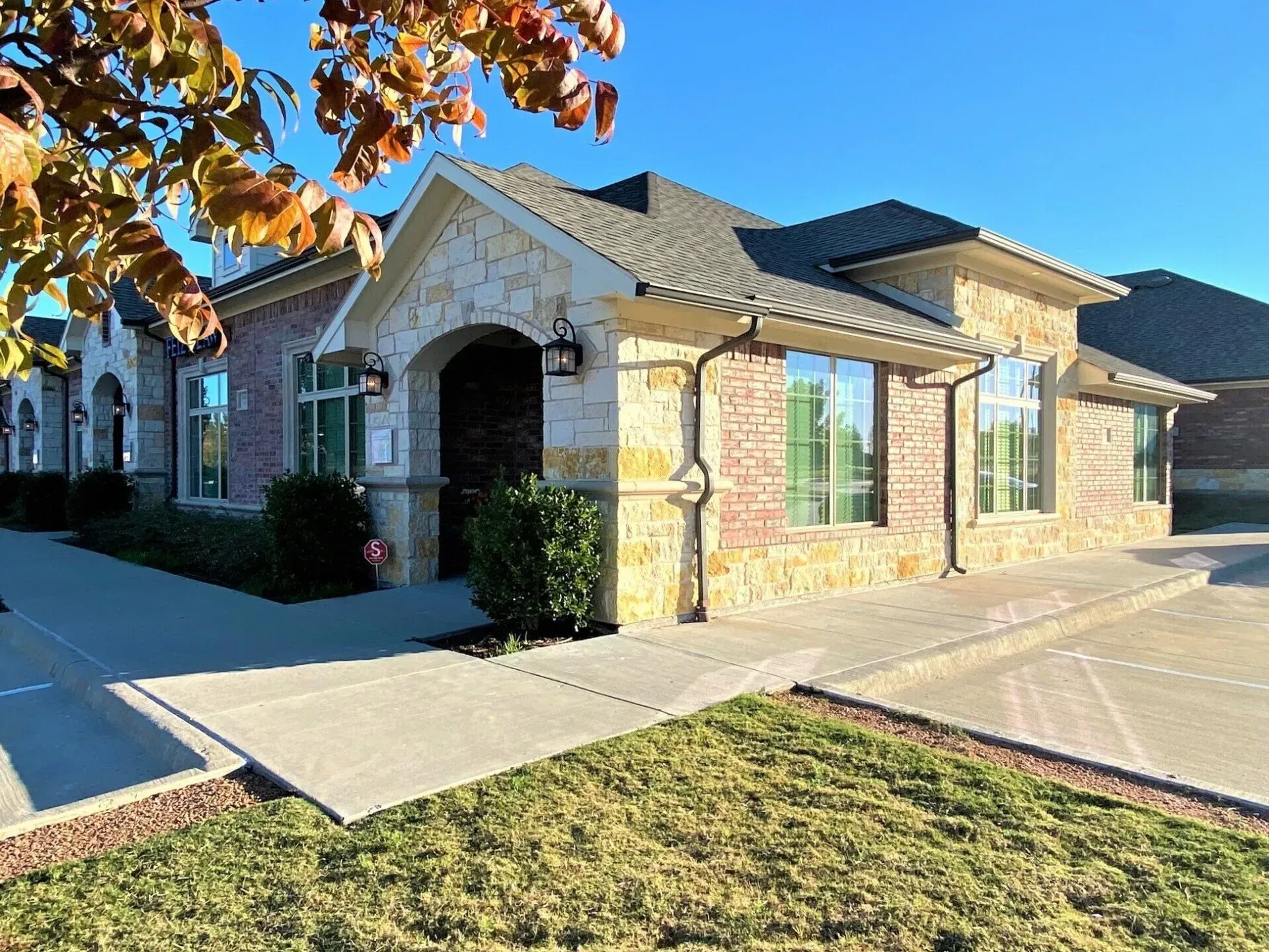 Single-story brick and stone building with arched entrance and large windows, on a sunny day.