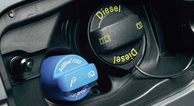Primo piano dello sportello del carburante con tappo nero del gasolio e tappo blu dell'AdBlue; entrambi etichettati.