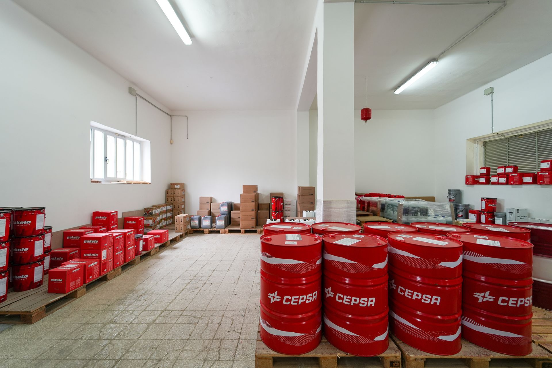 Interno del magazzino con fusti blu e scatole bianche su pallet e scaffali.