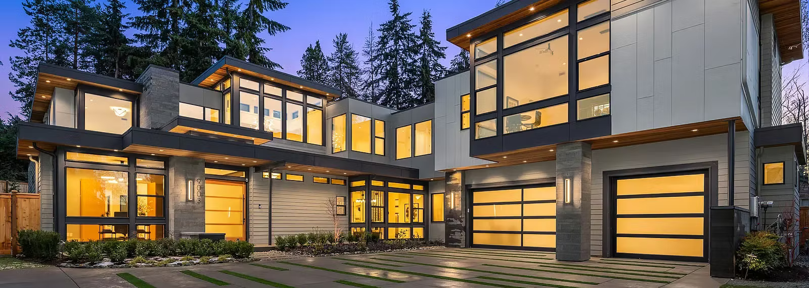 Modern two-story home with large windows and garage. Exterior lit in evening; landscaping.