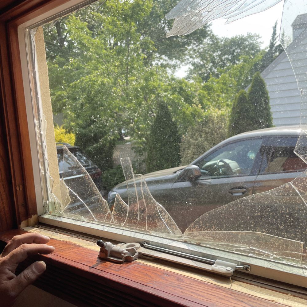 Broken window; brown wooden frame; gray car visible outside.