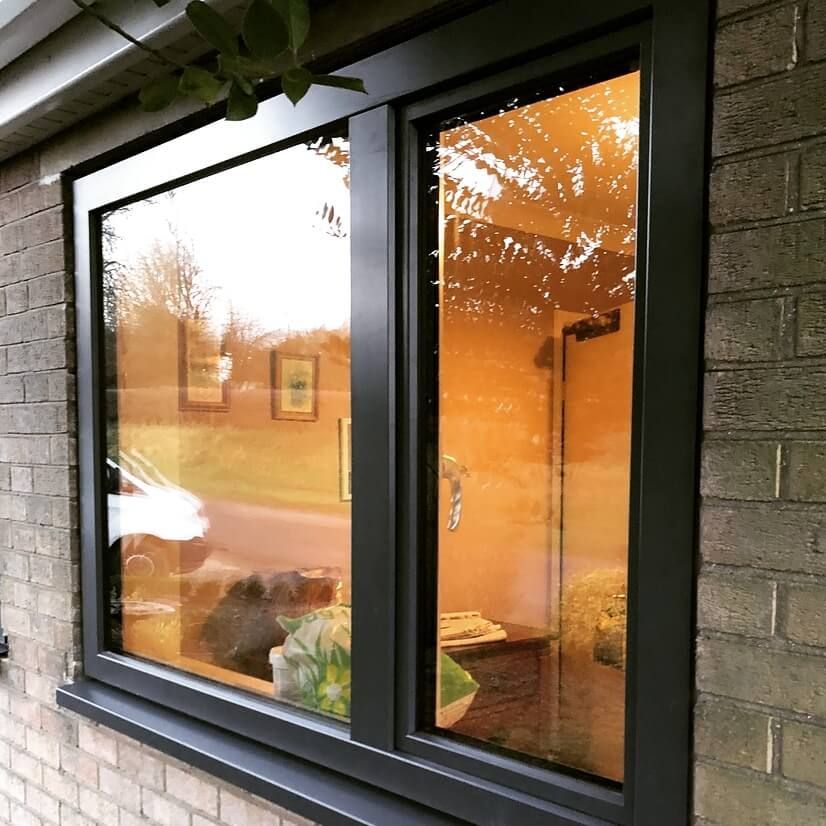 Black-framed double window reflecting an orange sunset and interior, set against a brick wall.