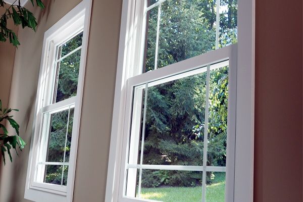 Two white framed, double-hung windows, one open, displaying a green yard, set against beige walls.