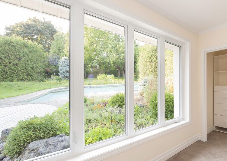 Large, multi-pane windows looking out onto a garden with a pool. White frames, natural light.
