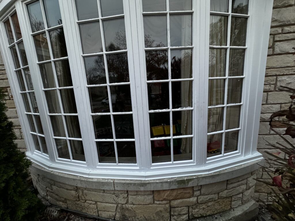 White framed bay window with multiple panes, set in stone wall.