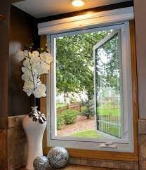 Open window with a white vase of flowers and two decorative balls; view of trees and lawn.