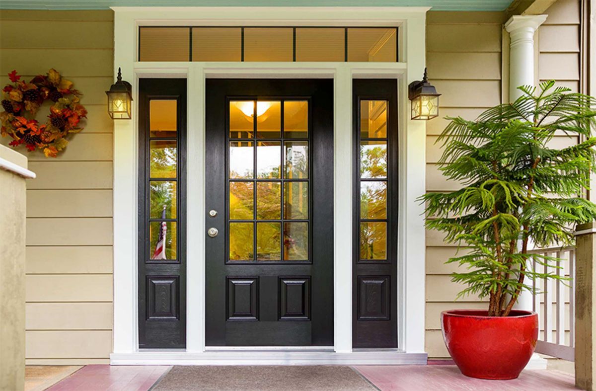 Black front door with sidelights and transom, flanked by lanterns and a potted plant.