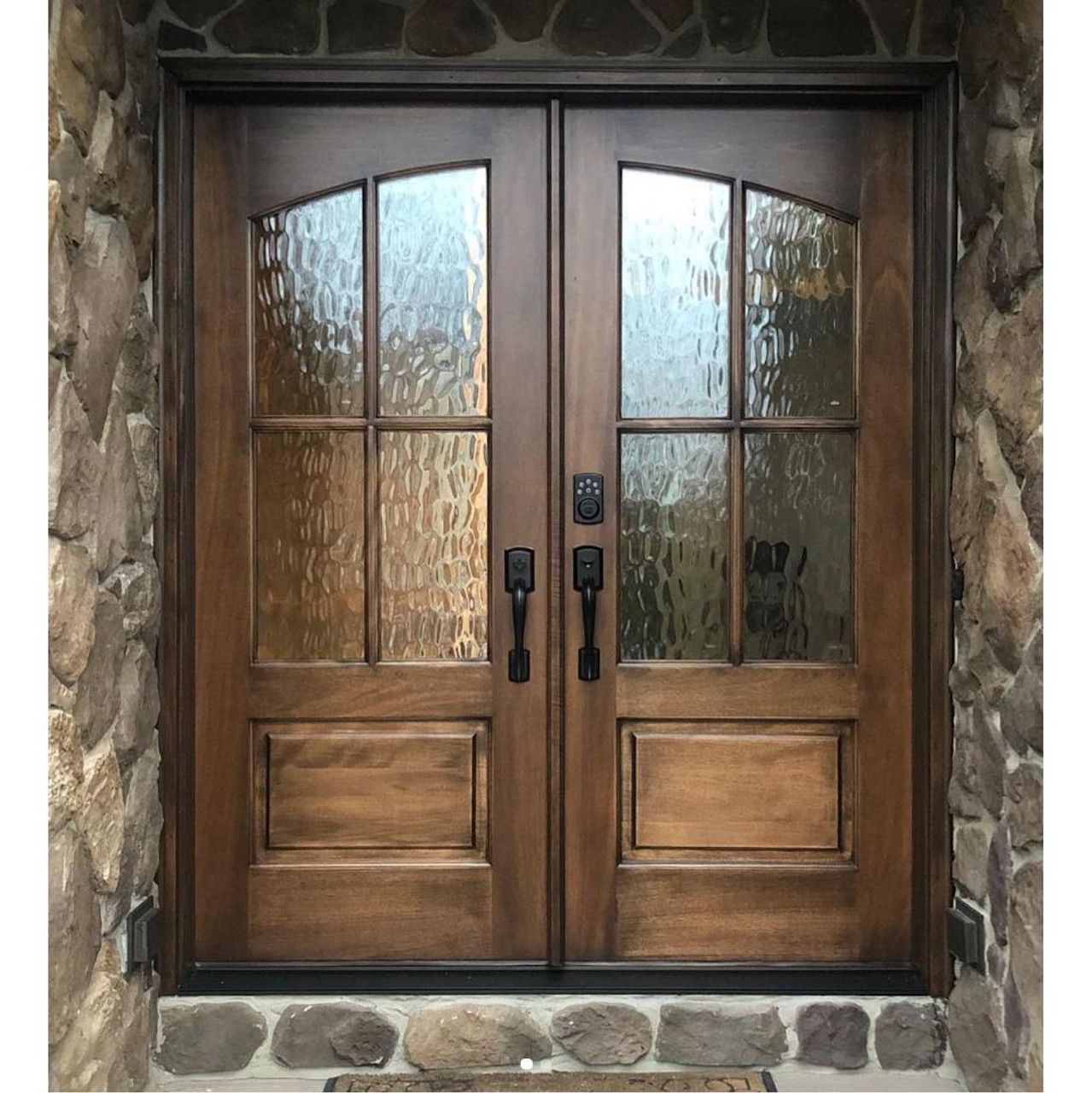 Wooden double doors with textured glass and dark hardware, set in a stone frame.