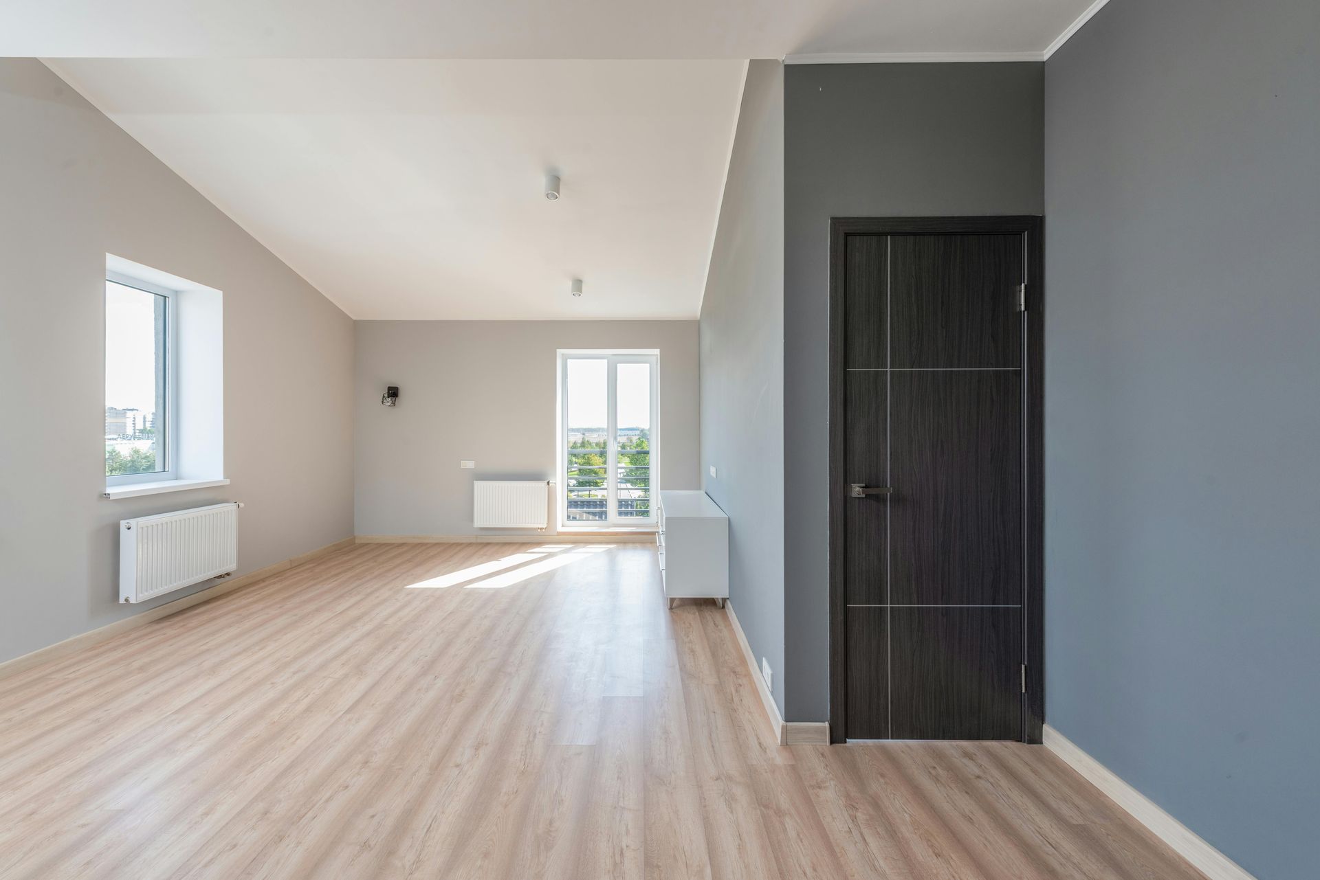 Empty modern room with gray walls, wooden floor, door, and window.
