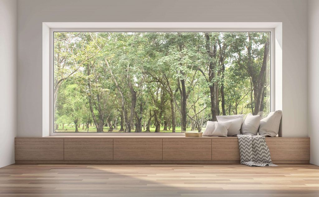 A large window overlooking a forest, with a built-in bench holding pillows and a blanket.
