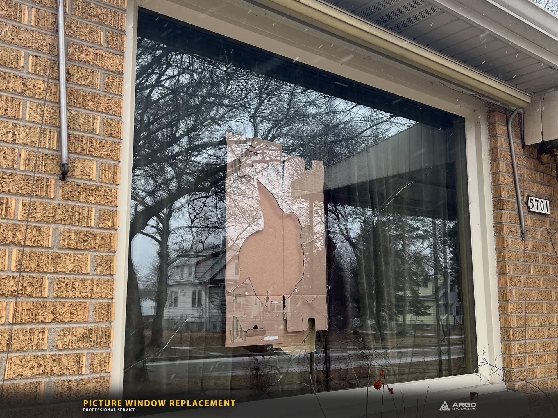 Broken window with cardboard covering the hole, brick building.