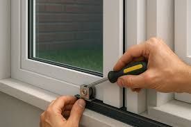 Person using a screwdriver to repair a window's sliding mechanism, close up, with white frame and green yard visible.
