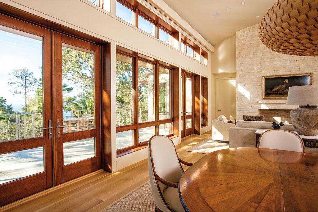 Elegant dining room with wooden doors and windows, views of trees, and a light-colored dining table.