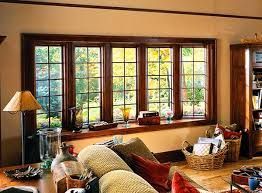 Living room with a dark wood framed window offering a view of trees, a sofa and side table with a lamp.