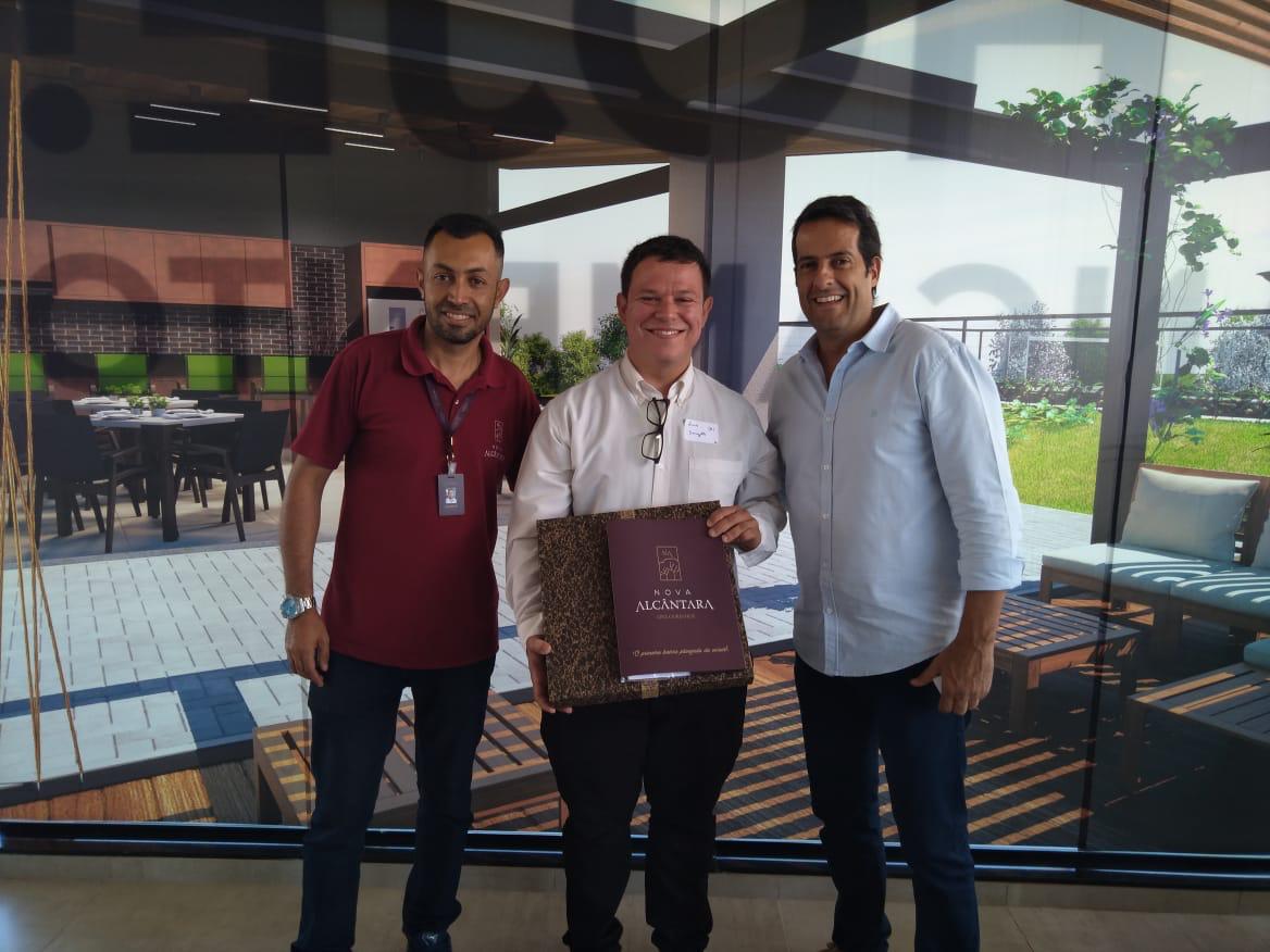 Três homens posam para uma foto em frente a uma grande janela