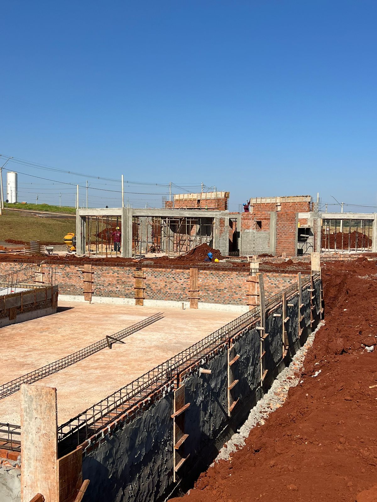 Um canteiro de obras com muita terra e prédios de tijolos ao fundo.