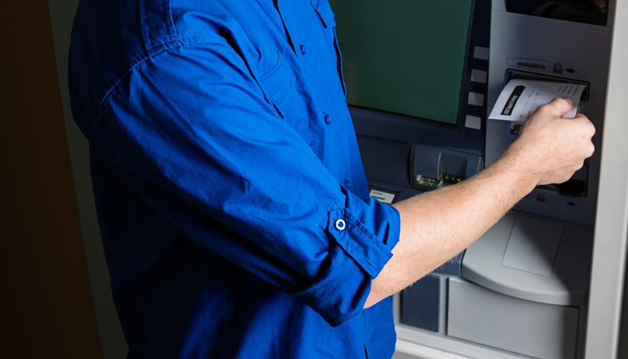 Um homem de camisa azul está usando um caixa eletrônico.