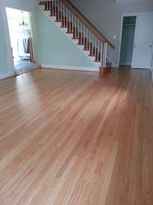 Empty living room with light wood floors, staircase, and doorway leading to a curtained room
