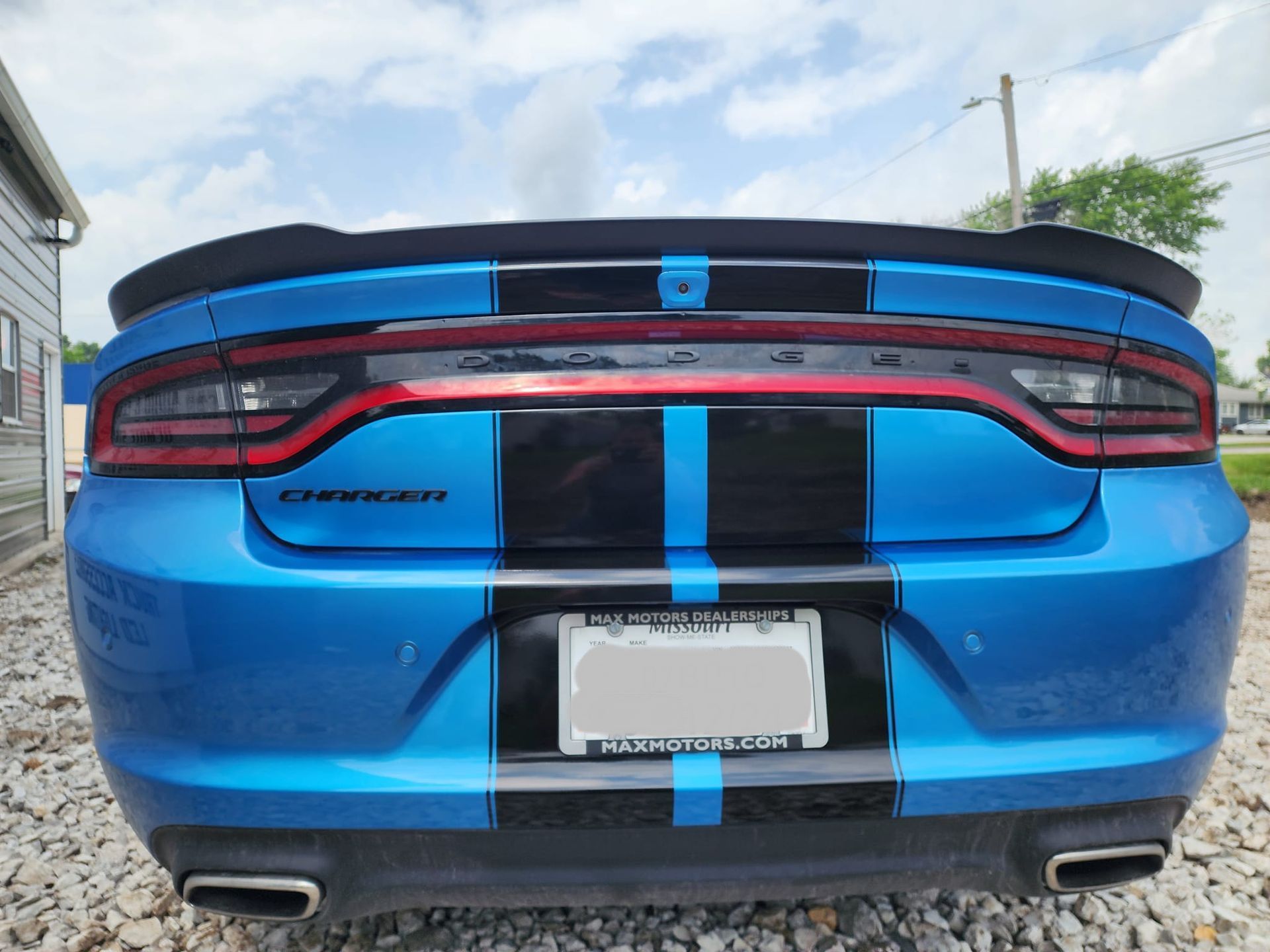 A blue dodge charger with black stripes is parked in front of a building.