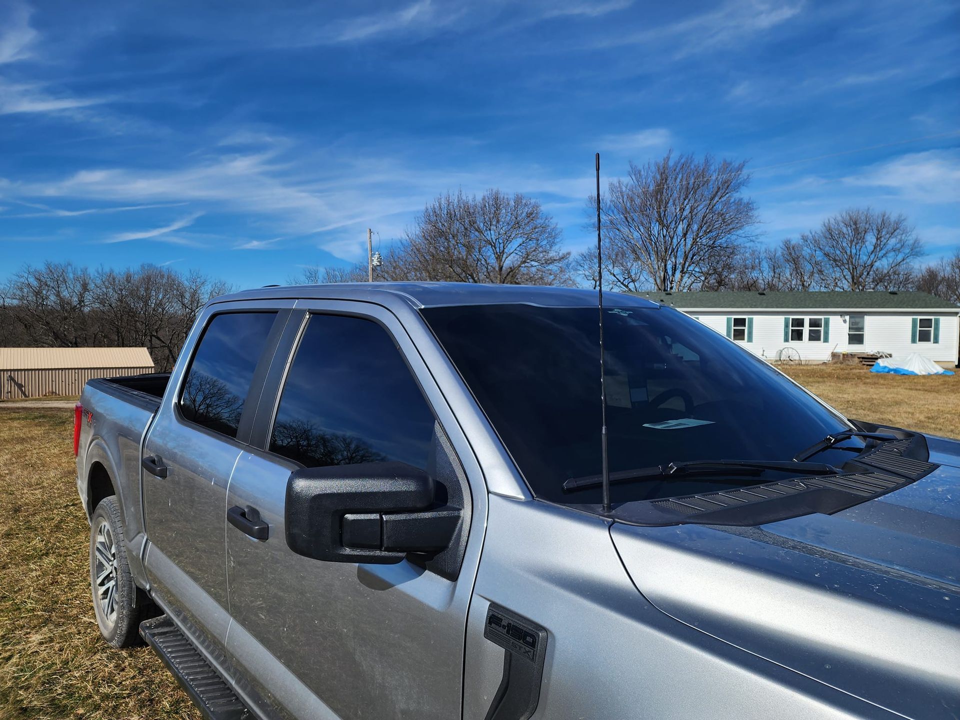 A silver truck is parked in a field with a house in the background.