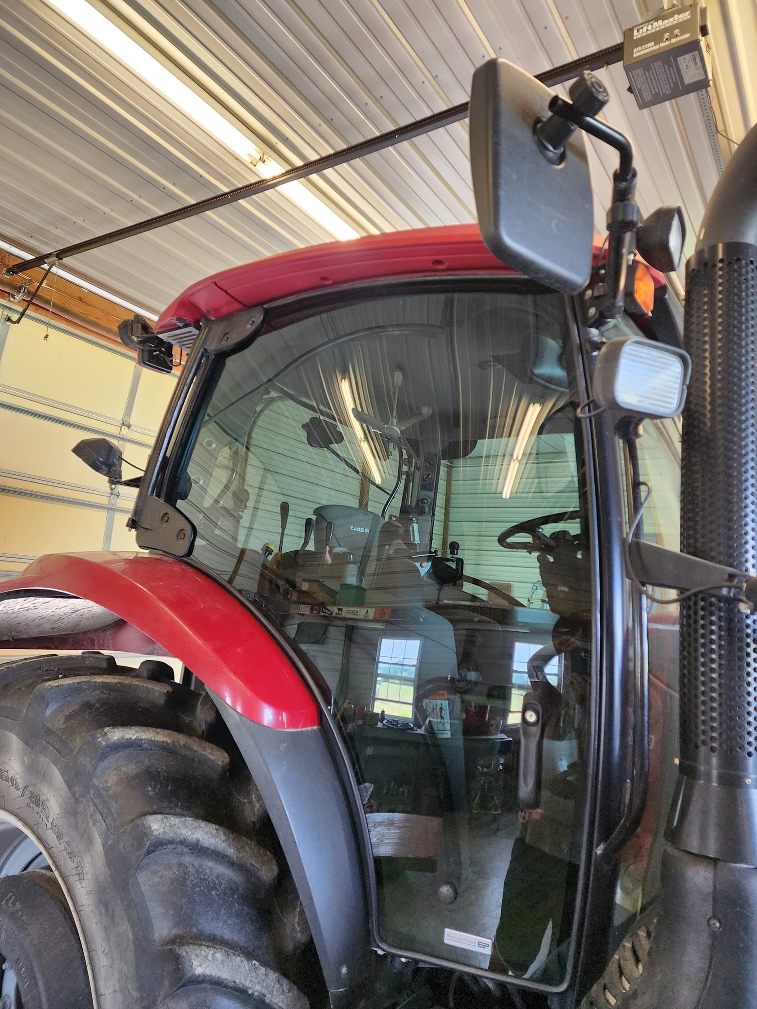 A blue tractor is parked in a garage with the windshield missing.