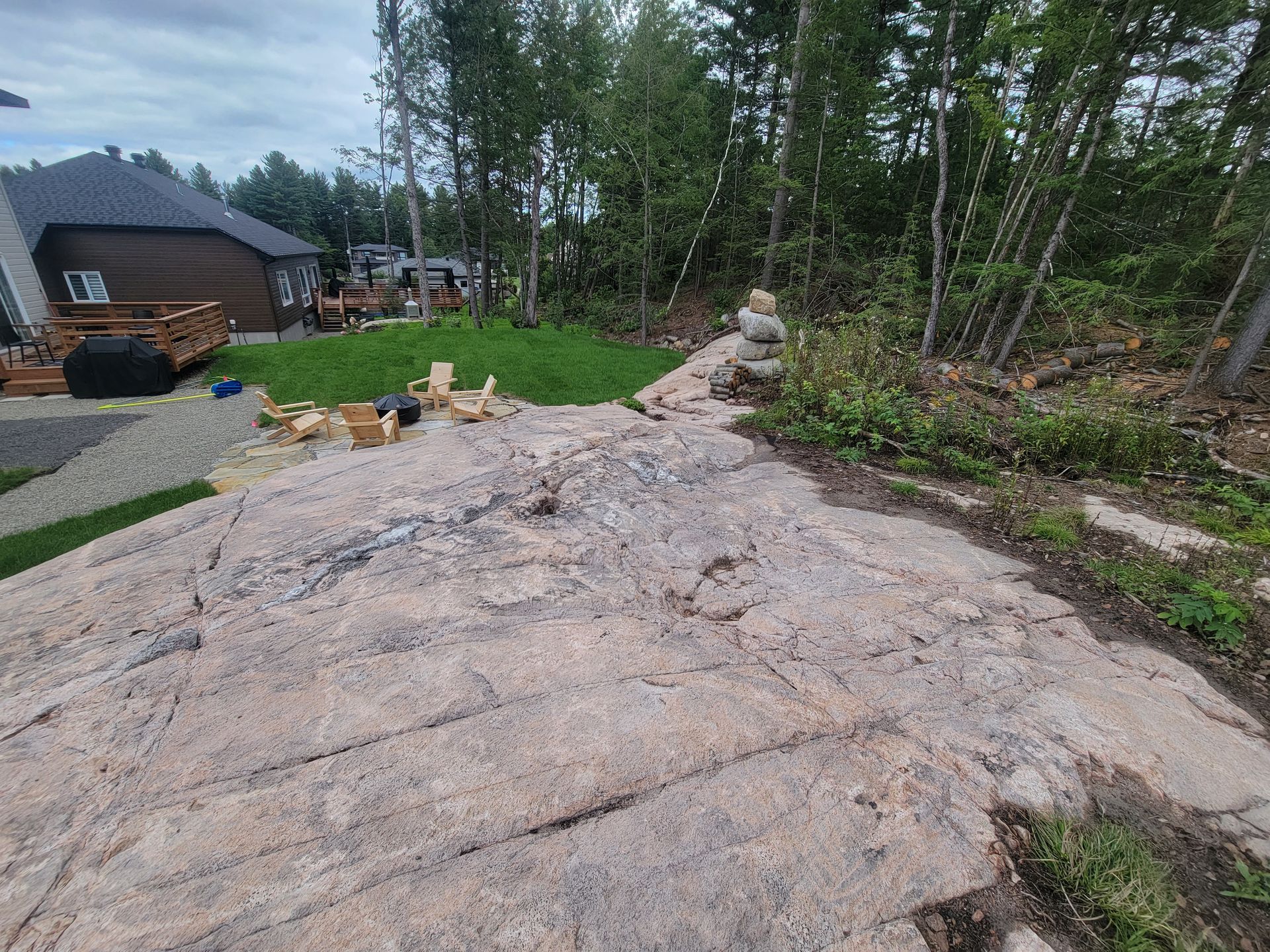 Un gros rocher au milieu d'une cour avec une maison en arrière-plan.