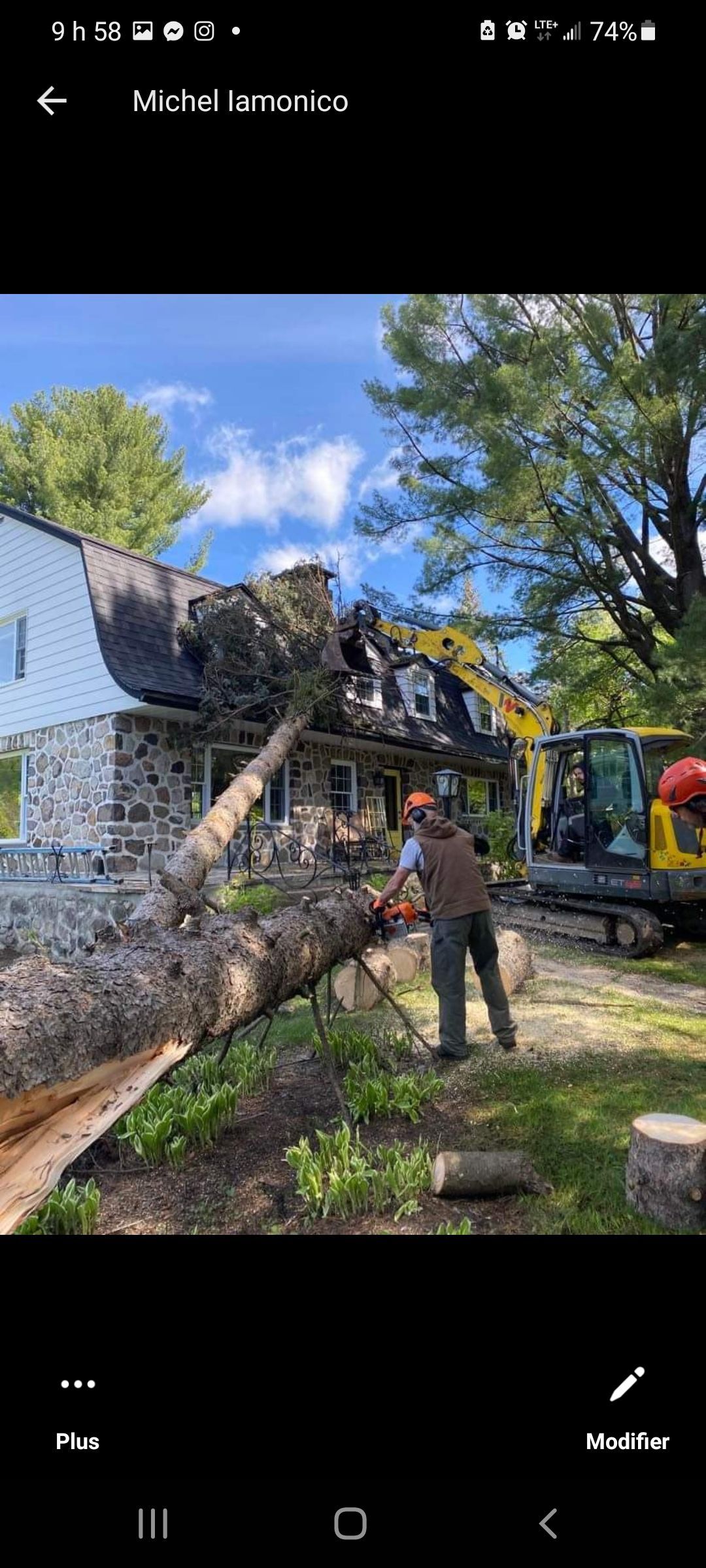 Un homme coupe un arbre devant une maison.